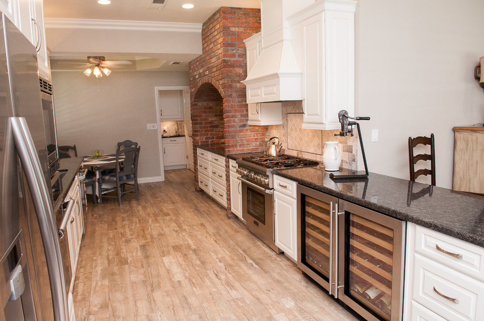 Mid-sized transitional galley porcelain tile and beige floor enclosed kitchen photo with a triple-bowl sink, raised-panel cabinets, white cabinets, granite countertops, beige backsplash, porcelain backsplash, stainless steel appliances and a peninsula