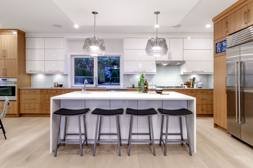 Photo of a contemporary l-shaped eat-in kitchen in Vancouver with an undermount sink, flat-panel cabinets, medium wood cabinets, white splashback, glass tile splashback, stainless steel appliances, light hardwood floors, with island, beige floor and white benchtop.