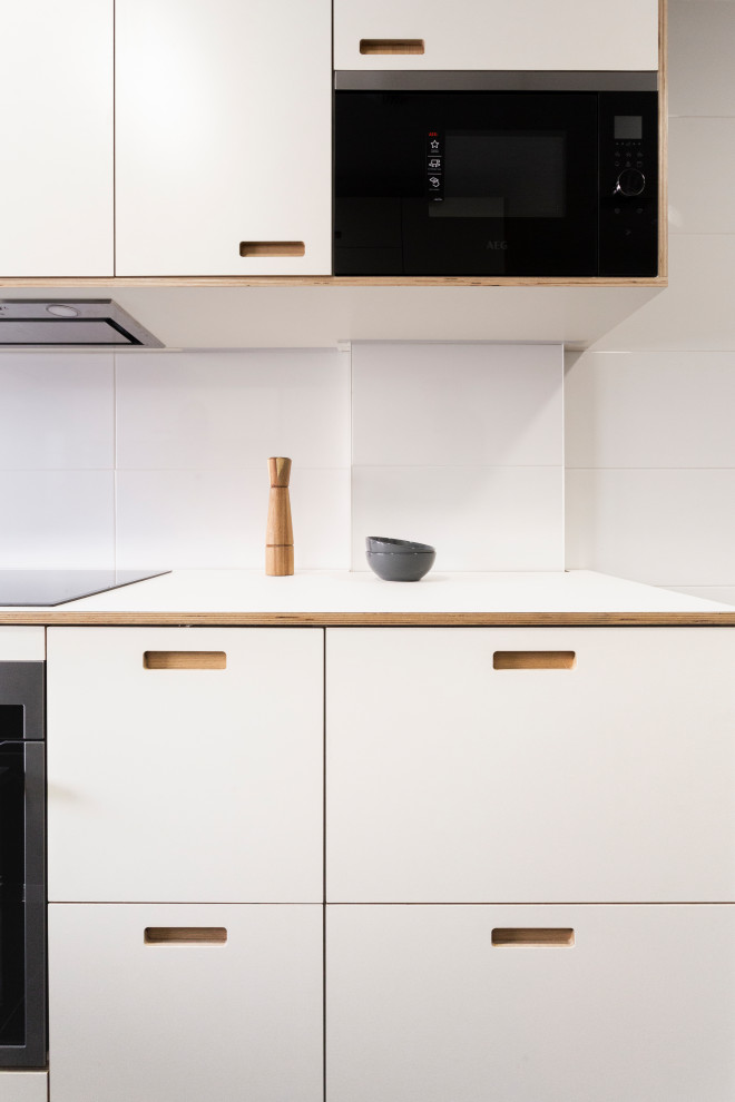 Inspiration for a mid-sized scandinavian u-shaped separate kitchen in Madrid with a drop-in sink, shaker cabinets, white cabinets, laminate benchtops, white splashback, ceramic splashback, stainless steel appliances, slate floors, no island, black floor, white benchtop and recessed.