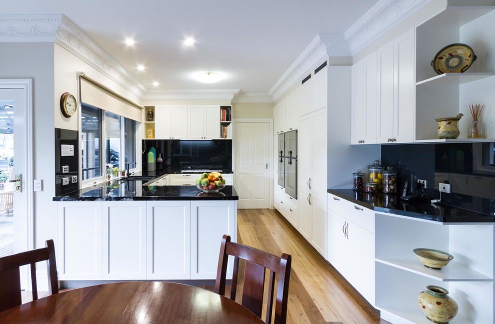 Inspiration for a large traditional u-shaped open plan kitchen in Melbourne with an undermount sink, shaker cabinets, white cabinets, granite benchtops, black splashback, ceramic splashback, stainless steel appliances, light hardwood floors and brown floor.