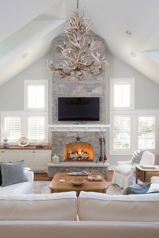 Photo of a beach style family room in Milwaukee with grey walls, a standard fireplace, a stone fireplace surround and a wall-mounted tv.