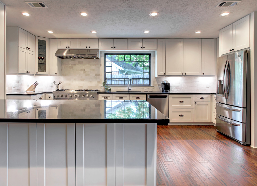 Design ideas for an expansive transitional galley open plan kitchen in Houston with a single-bowl sink, shaker cabinets, white cabinets, granite benchtops, white splashback, travertine splashback, stainless steel appliances, bamboo floors, with island, brown floor and black benchtop.