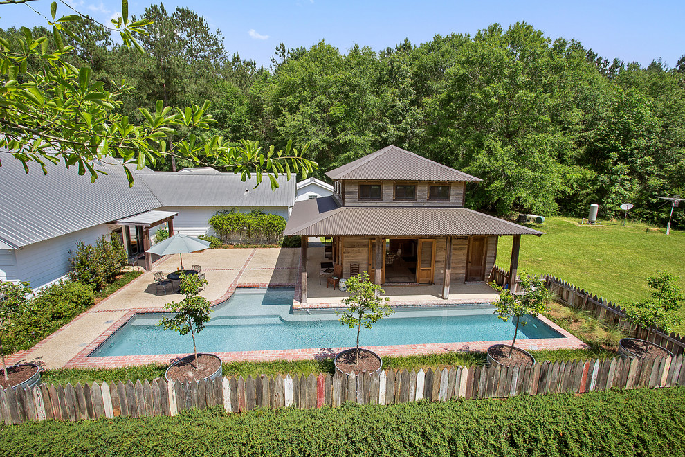 Photo of a mid-sized country backyard custom-shaped lap pool in New Orleans with a pool house and brick pavers.