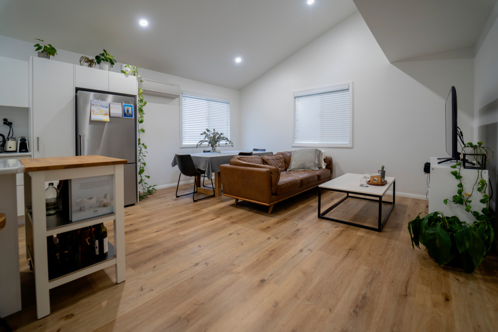 Ejemplo de salón abierto y abovedado contemporáneo de tamaño medio con paredes blancas, suelo laminado, televisor independiente y suelo marrón