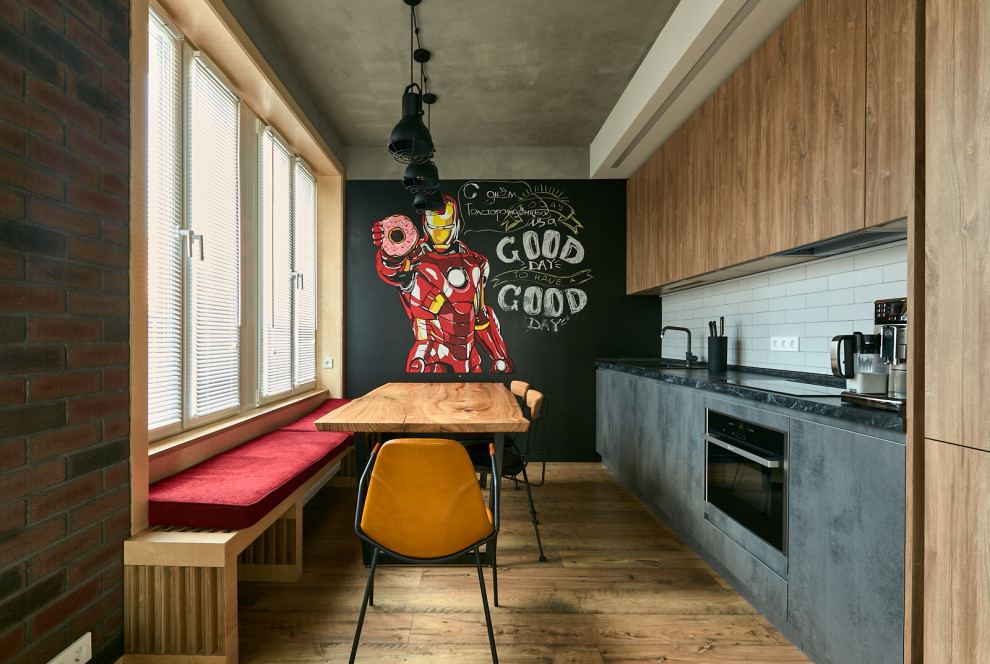 This is an example of an industrial single-wall eat-in kitchen in Moscow with a drop-in sink, flat-panel cabinets, grey cabinets, white splashback, stainless steel appliances, medium hardwood floors, brown floor, black benchtop, no island and recessed.