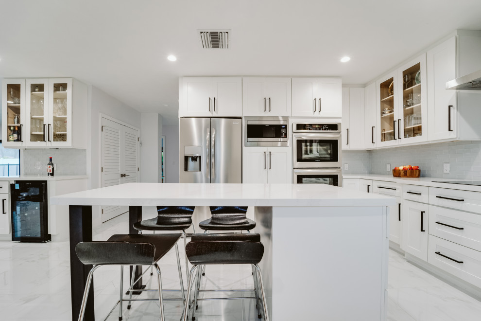 Inspiration for a large modern u-shaped eat-in kitchen in Miami with an undermount sink, shaker cabinets, white cabinets, grey splashback, glass tile splashback, stainless steel appliances, ceramic floors, with island, grey floor and white benchtop.