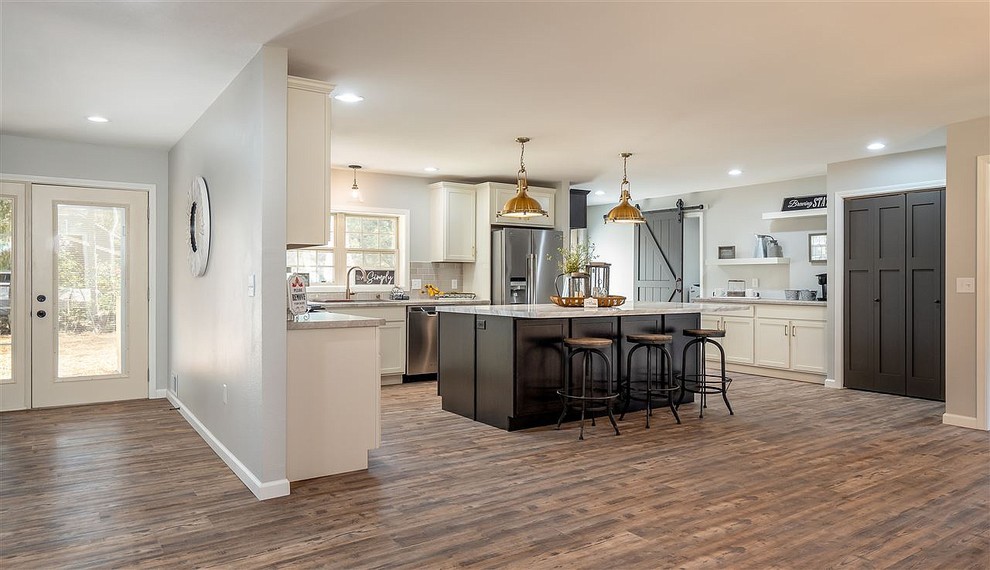 This is an example of a large country u-shaped eat-in kitchen in Other with a farmhouse sink, shaker cabinets, laminate benchtops, grey splashback, subway tile splashback, stainless steel appliances, light hardwood floors, with island, brown floor, multi-coloured benchtop and white cabinets.