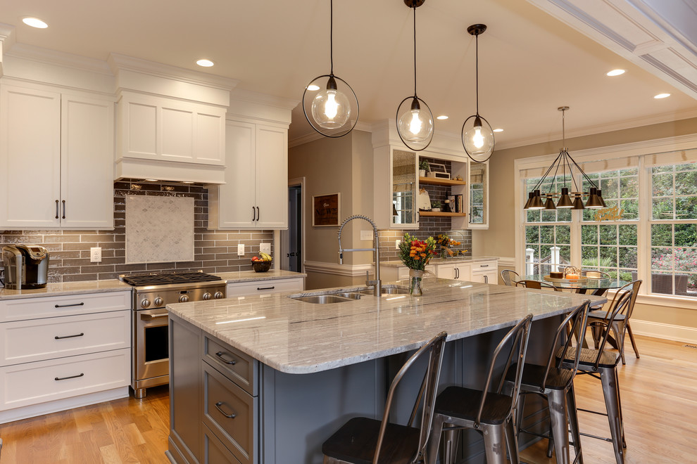 This is an example of a mid-sized transitional eat-in kitchen in Raleigh with a triple-bowl sink, white cabinets, granite benchtops, grey splashback, stainless steel appliances, with island, grey benchtop, shaker cabinets, subway tile splashback and light hardwood floors.