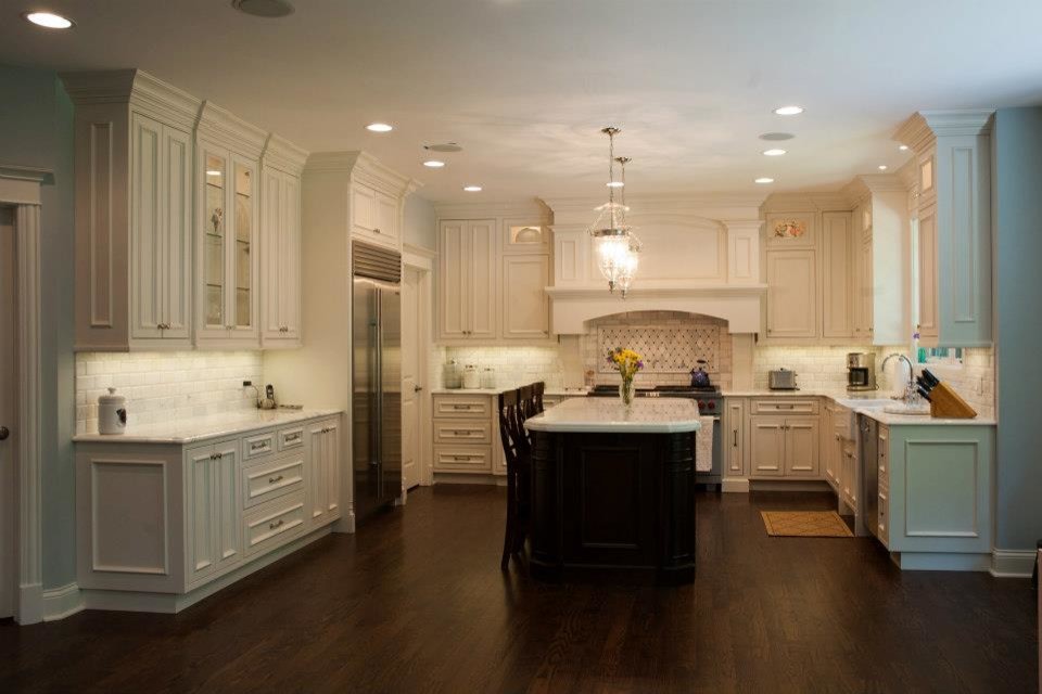 Large transitional u-shaped dark wood floor and brown floor kitchen photo in Chicago with a farmhouse sink, recessed-panel cabinets, white cabinets, quartzite countertops, gray backsplash, subway tile backsplash, stainless steel appliances and an island