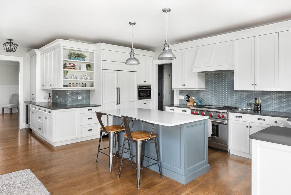Mid-sized transitional u-shaped open plan kitchen in Chicago with a farmhouse sink, beaded inset cabinets, white cabinets, quartz benchtops, blue splashback, porcelain splashback, panelled appliances, with island, brown floor, white benchtop and dark hardwood floors.