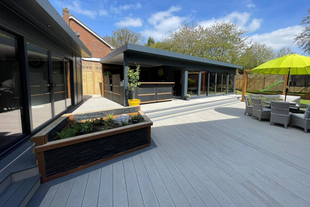 Design ideas for a large modern backyard and ground level deck in Hertfordshire with an outdoor kitchen and a roof extension.