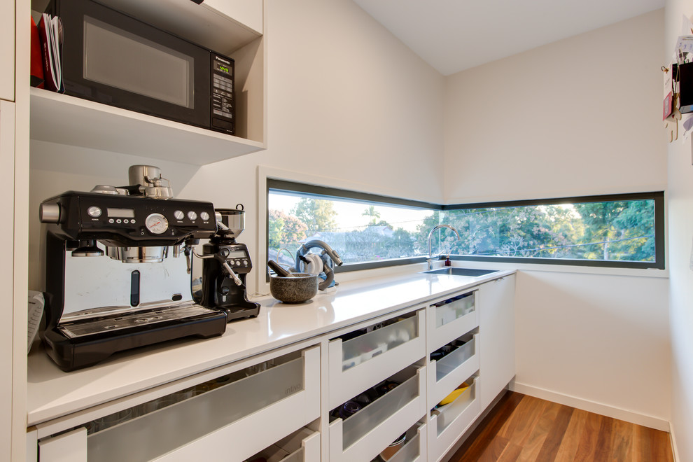 Photo of a mid-sized contemporary galley eat-in kitchen in Brisbane with a drop-in sink, flat-panel cabinets, white cabinets, limestone benchtops, yellow splashback, ceramic splashback, stainless steel appliances, light hardwood floors, with island, brown floor and white benchtop.