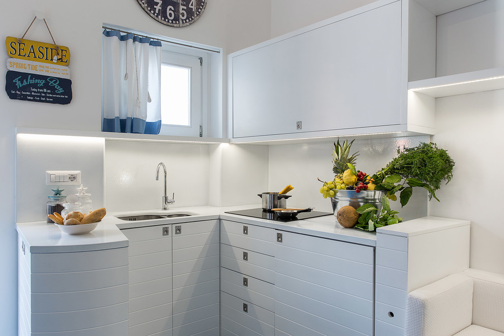 Small beach style l-shaped kitchen in Naples with a double-bowl sink, white cabinets and white splashback.