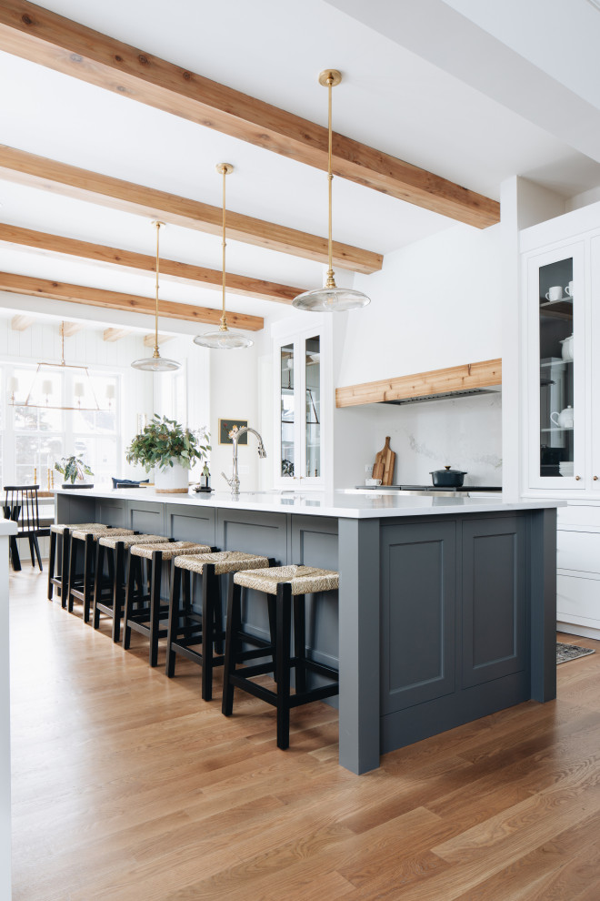 Country galley eat-in kitchen in Chicago with shaker cabinets, white cabinets, white splashback, medium hardwood floors, with island, brown floor, white benchtop and exposed beam.