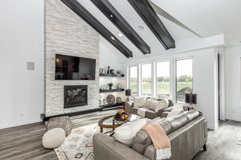 Diseño de sala de estar abierta y abovedada de estilo de casa de campo con paredes blancas, suelo laminado, todas las chimeneas, marco de chimenea de piedra, televisor colgado en la pared y suelo gris