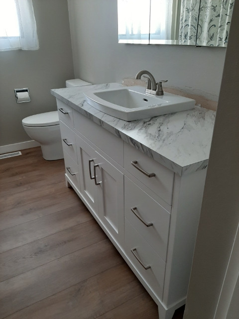 Example of a small transitional gray tile laminate floor, brown floor and single-sink alcove bathtub design with shaker cabinets, white cabinets, a two-piece toilet, gray walls, a drop-in sink, laminate countertops, multicolored countertops and a freestanding vanity