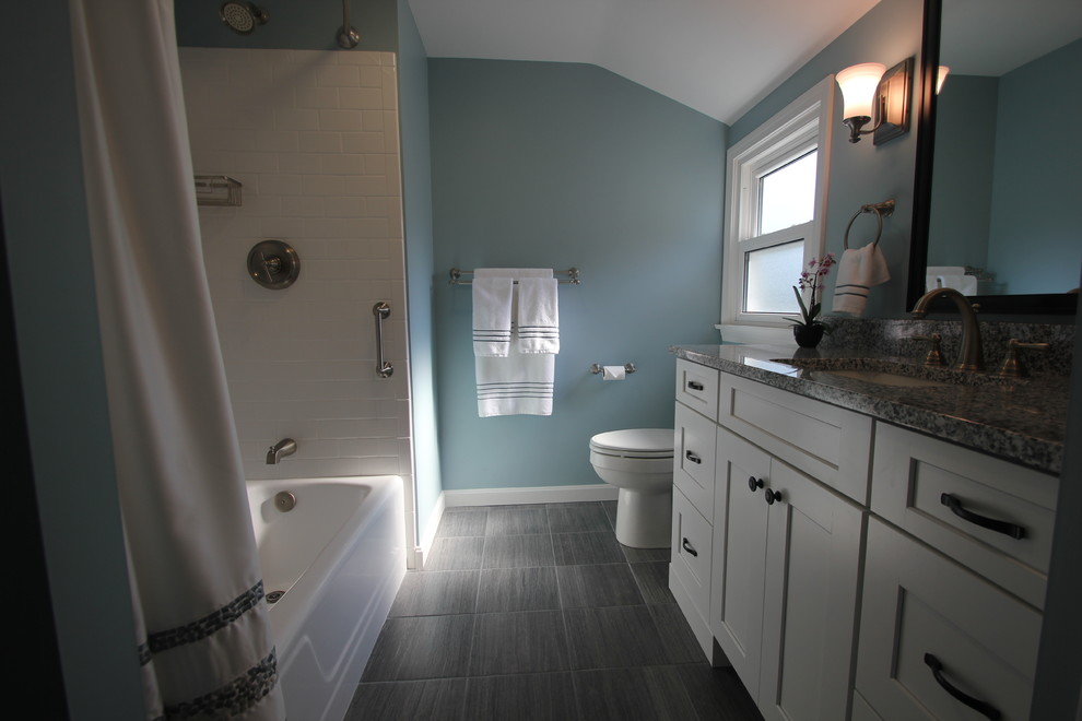 Photo of a mid-sized traditional bathroom in Cleveland with shaker cabinets, white cabinets, an alcove tub, a shower/bathtub combo, blue walls, an undermount sink, granite benchtops, white tile, subway tile, porcelain floors, grey floor and a shower curtain.
