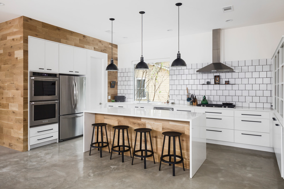 This is an example of a mid-sized scandinavian u-shaped eat-in kitchen in Austin with flat-panel cabinets, white cabinets, white splashback, ceramic splashback, stainless steel appliances, concrete floors, with island, grey floor and white benchtop.