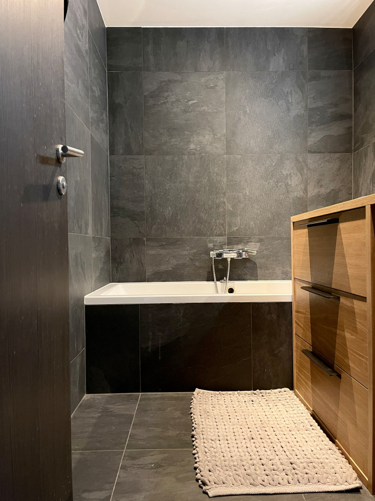 Photo of a mid-sized contemporary master bathroom in Lyon with light wood cabinets, a drop-in tub, black tile, stone tile, black walls, ceramic floors, a console sink, wood benchtops, black floor and a single vanity.