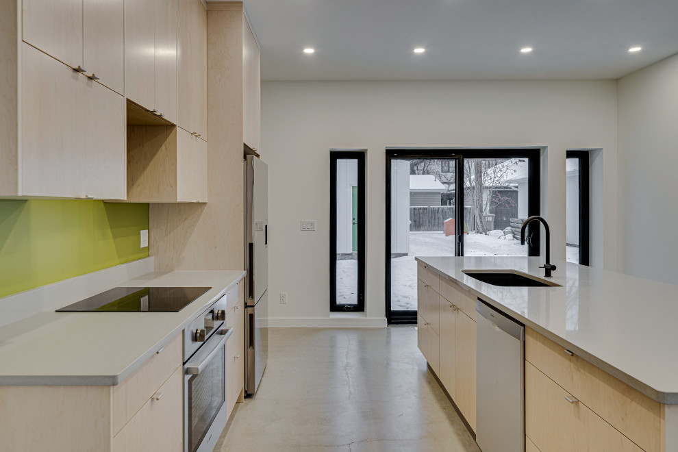 Immagine di una cucina moderna di medie dimensioni con lavello sottopiano, ante lisce, ante in legno chiaro, top in quarzite, paraspruzzi verde, elettrodomestici in acciaio inossidabile, pavimento in cemento, pavimento grigio e top bianco