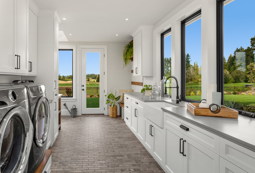 Photo of an expansive country l-shaped utility room in Portland with a farmhouse sink, shaker cabinets, white cabinets, quartz benchtops, white walls, ceramic floors, a side-by-side washer and dryer, grey floor and grey benchtop.