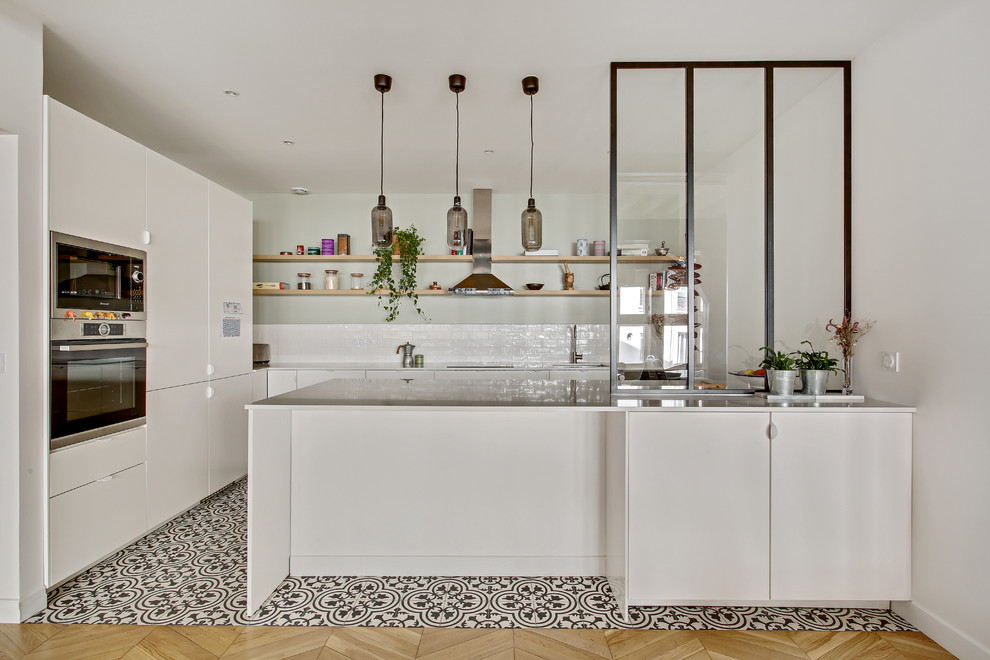 Design ideas for a transitional l-shaped eat-in kitchen in Paris with an undermount sink, flat-panel cabinets, white cabinets, white splashback, subway tile splashback, stainless steel appliances, cement tiles, a peninsula, multi-coloured floor and white benchtop.