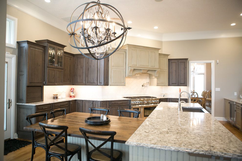 Inspiration for a large transitional u-shaped medium tone wood floor and brown floor kitchen remodel in Indianapolis with a farmhouse sink, raised-panel cabinets, dark wood cabinets, granite countertops, white backsplash, subway tile backsplash, paneled appliances, an island and multicolored countertops
