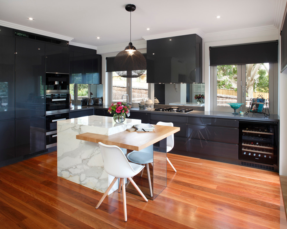 Mid-sized contemporary l-shaped eat-in kitchen in Sydney with an undermount sink, recessed-panel cabinets, grey cabinets, marble benchtops, metallic splashback, mirror splashback, black appliances, light hardwood floors and with island.