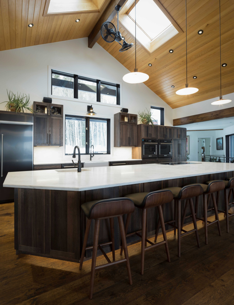 Photo of an expansive traditional single-wall open plan kitchen in Denver with a belfast sink, shaker cabinets, dark wood cabinets, marble worktops, integrated appliances, dark hardwood flooring, an island, brown floors, white worktops and a timber clad ceiling.