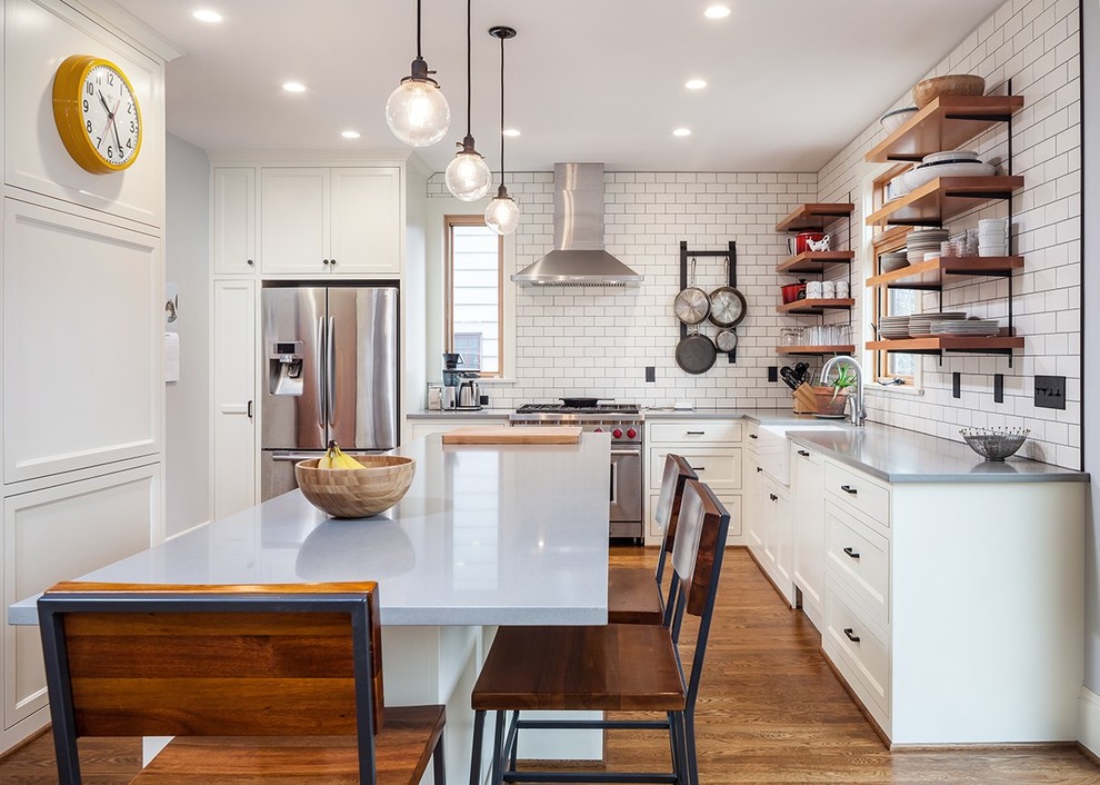 Design ideas for a mid-sized country l-shaped eat-in kitchen in Portland with a farmhouse sink, white cabinets, solid surface benchtops, white splashback, subway tile splashback, stainless steel appliances, with island, open cabinets, medium hardwood floors and brown floor.