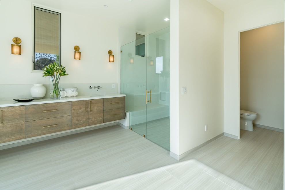 Design ideas for a large contemporary master bathroom in Santa Barbara with flat-panel cabinets, medium wood cabinets, a freestanding tub, a curbless shower, a one-piece toilet, white walls, porcelain floors, an undermount sink, engineered quartz benchtops, white floor, a hinged shower door and white benchtops.