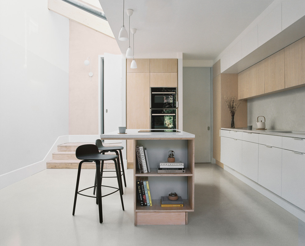 Photo of a mid-sized modern single-wall open plan kitchen in Other with a drop-in sink, flat-panel cabinets, light wood cabinets, quartz benchtops, grey splashback, engineered quartz splashback, black appliances, concrete floors, with island, pink floor, white benchtop and exposed beam.