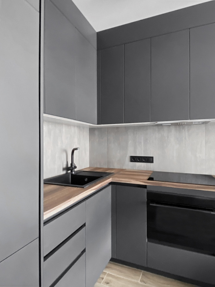 Mid-sized contemporary l-shaped eat-in kitchen in Moscow with a single-bowl sink, flat-panel cabinets, black cabinets, wood benchtops, grey splashback, stone slab splashback, panelled appliances, porcelain floors, no island, beige floor and beige benchtop.
