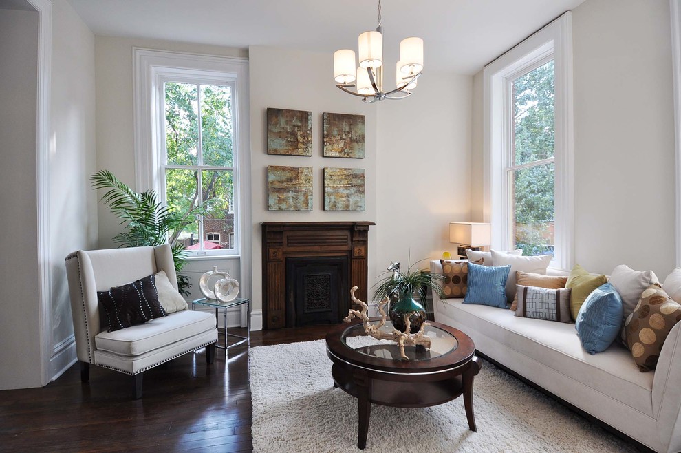 This is an example of a small traditional enclosed living room in St Louis with white walls, a standard fireplace, a wood fireplace surround and dark hardwood floors.