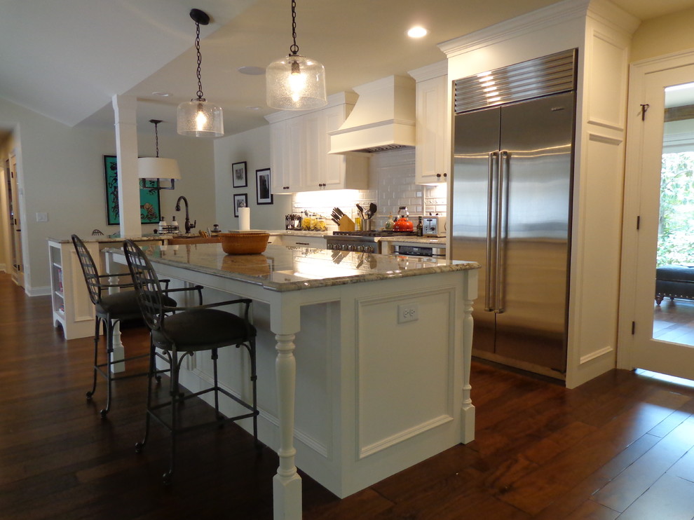 Open concept kitchen - large transitional u-shaped dark wood floor open concept kitchen idea in Raleigh with a farmhouse sink, recessed-panel cabinets, white cabinets, granite countertops, white backsplash, subway tile backsplash, stainless steel appliances and an island