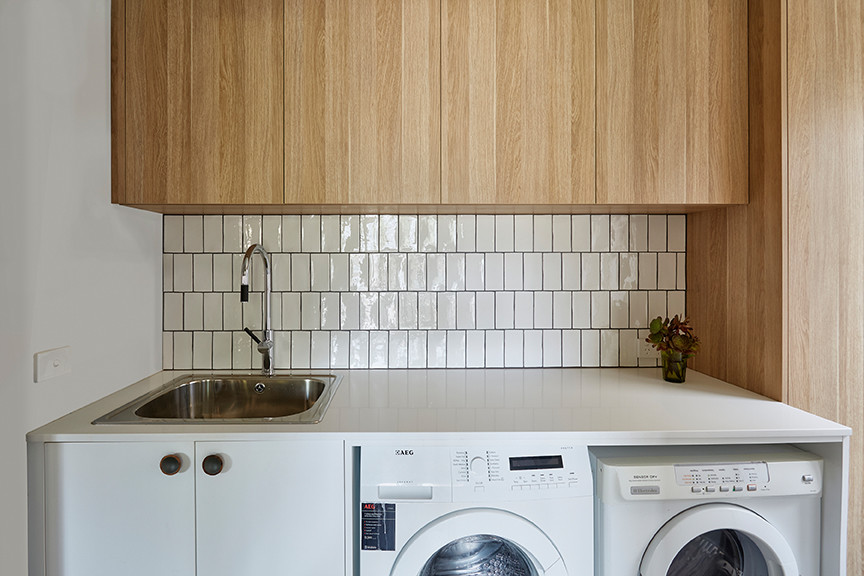 Inspiration for a mid-sized contemporary single-wall dedicated laundry room in Melbourne with a farmhouse sink, raised-panel cabinets, light wood cabinets, solid surface benchtops, slate floors and a side-by-side washer and dryer.