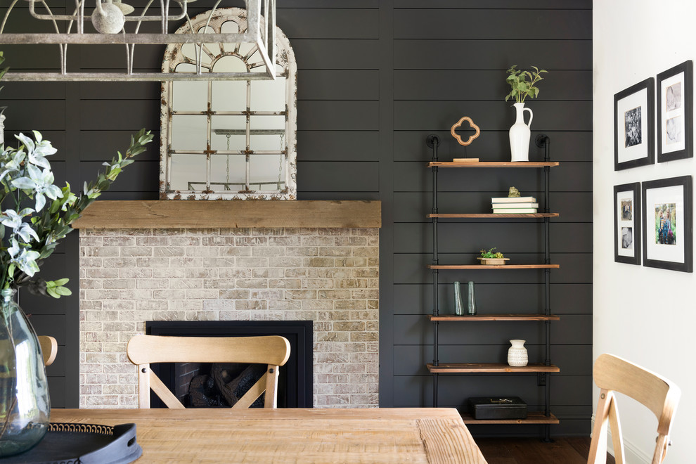 Photo of a mid-sized country kitchen/dining combo in Minneapolis with black walls, medium hardwood floors, a standard fireplace, a brick fireplace surround and brown floor.