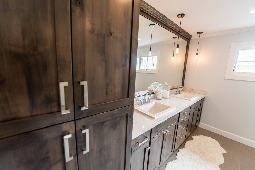 This is an example of a large transitional master bathroom in Portland with recessed-panel cabinets, dark wood cabinets, a double shower, a one-piece toilet, grey walls, porcelain floors, a drop-in sink, marble benchtops, beige floor and a hinged shower door.