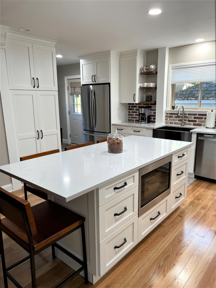 Inspiration for a large transitional l-shaped eat-in kitchen in Detroit with an undermount sink, shaker cabinets, white cabinets, quartz benchtops, multi-coloured splashback, brick splashback, stainless steel appliances, light hardwood floors, with island, brown floor and grey benchtop.