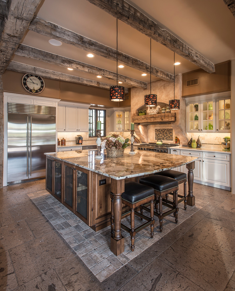 Example of a large mountain style l-shaped travertine floor open concept kitchen design in Phoenix with a farmhouse sink, raised-panel cabinets, white cabinets, granite countertops, beige backsplash, stone tile backsplash, stainless steel appliances and an island