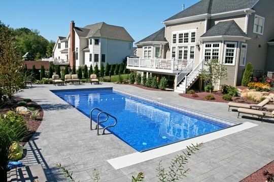 Example of a mid-sized backyard stamped concrete and rectangular pool design in Boston