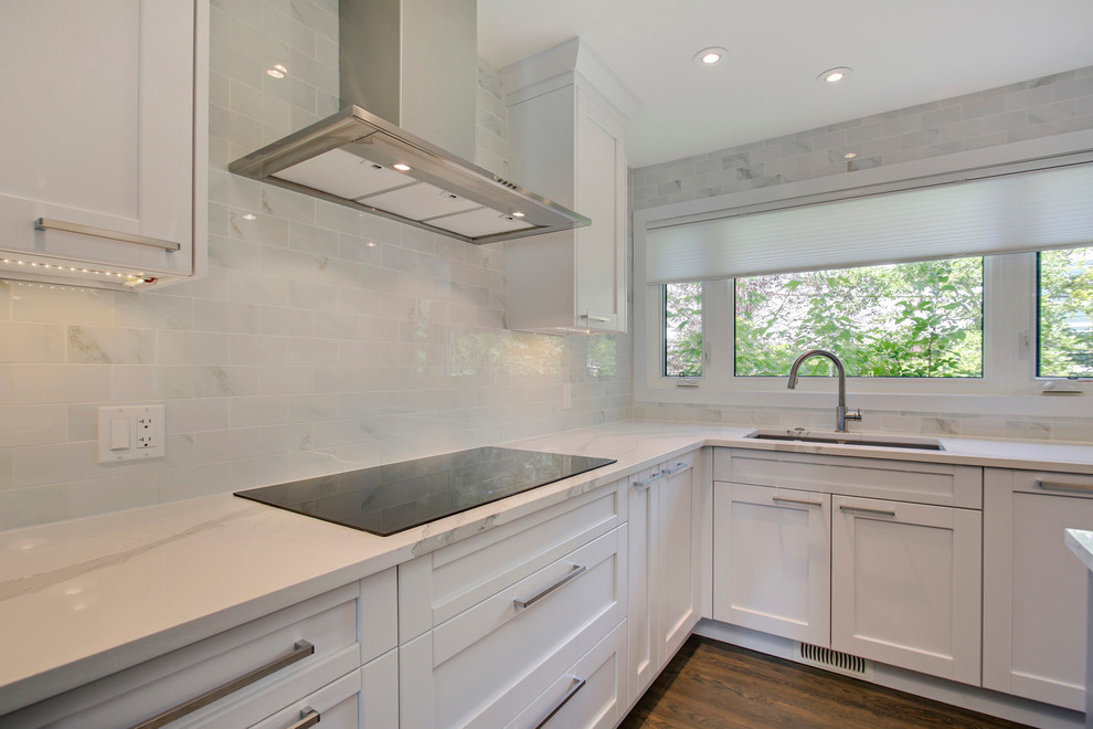 Example of a transitional l-shaped medium tone wood floor eat-in kitchen design in Calgary with an undermount sink, shaker cabinets, white cabinets, quartz countertops, white backsplash, porcelain backsplash, stainless steel appliances and an island