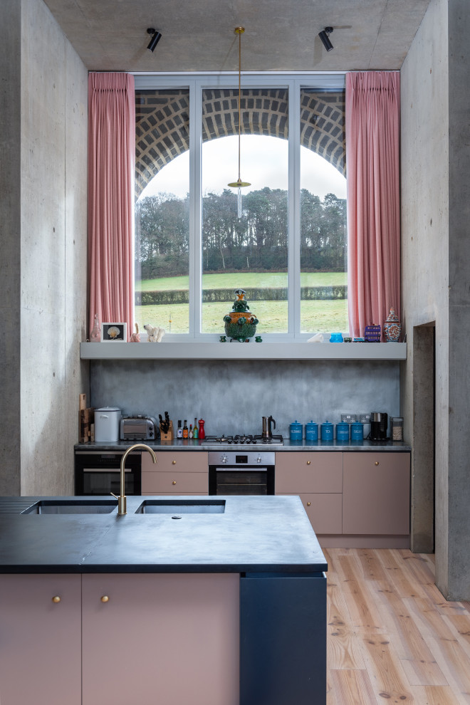 Cette photo montre une grande cuisine ouverte tendance avec un évier posé, un placard à porte plane, des portes de placard rose, un électroménager en acier inoxydable, un sol en bois brun, îlot, un sol beige et plan de travail noir.