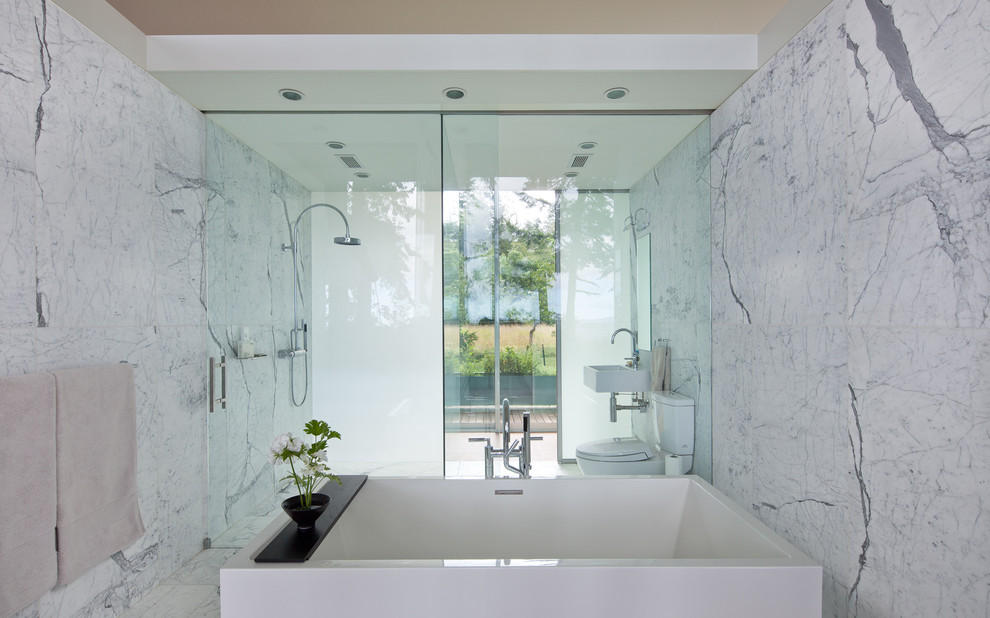 Design ideas for a large modern master bathroom in Seattle with a wall-mount sink, a freestanding tub, a two-piece toilet, white tile, stone tile, grey walls and marble floors.