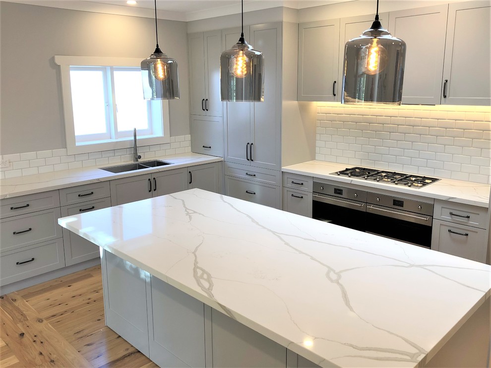 Inspiration for a mid-sized transitional l-shaped kitchen in Sydney with an undermount sink, shaker cabinets, grey cabinets, quartz benchtops, subway tile splashback, stainless steel appliances, light hardwood floors and with island.