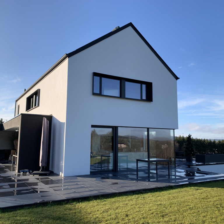 Cette image montre une façade de maison beige minimaliste en planches et couvre-joints de taille moyenne et à deux étages et plus avec un toit à deux pans, un toit mixte et un toit noir.