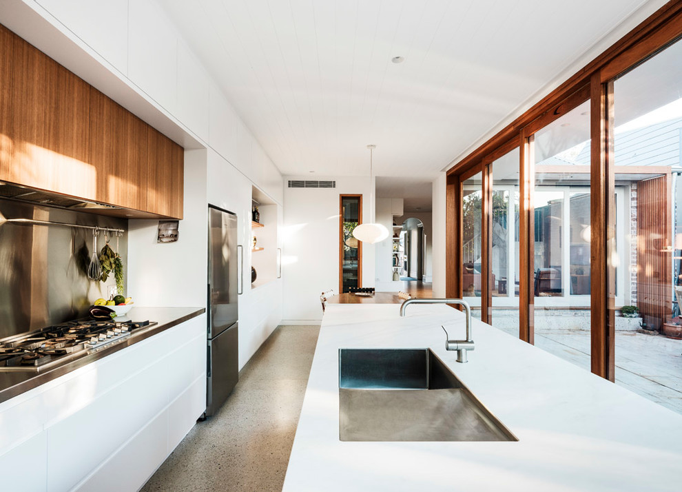 Photo of a large contemporary galley eat-in kitchen in Sydney with a drop-in sink, flat-panel cabinets, white cabinets, quartz benchtops, metallic splashback, metal splashback, stainless steel appliances, concrete floors, with island, grey floor and white benchtop.