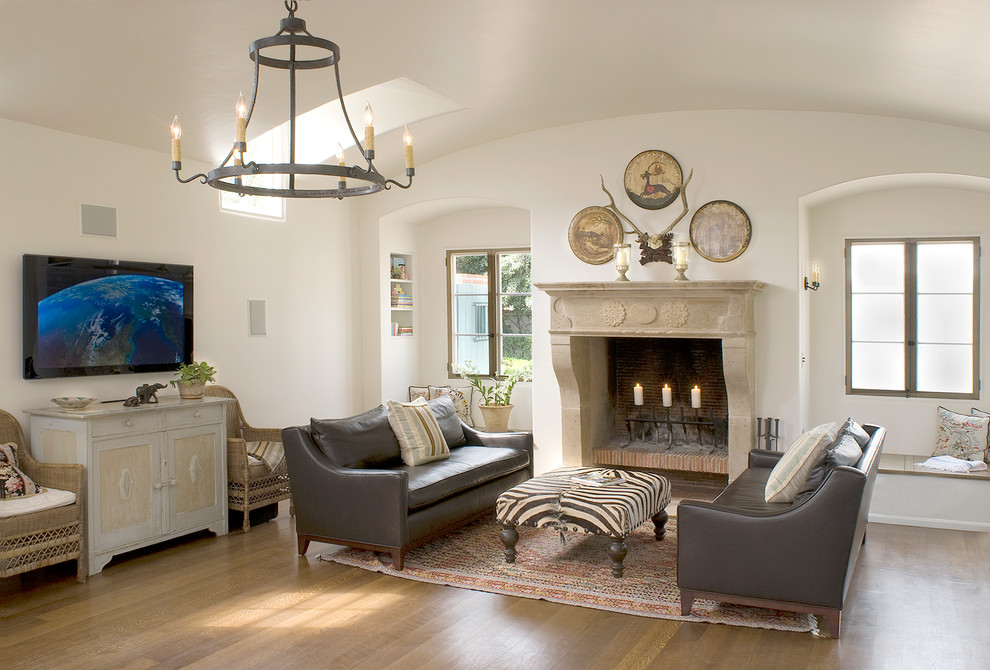 This is an example of a large mediterranean open concept family room in Santa Barbara with white walls, medium hardwood floors, a standard fireplace and a stone fireplace surround.