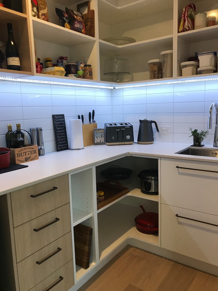 Large contemporary galley open plan kitchen in Christchurch with a single-bowl sink, flat-panel cabinets, white cabinets, quartz benchtops, grey splashback, stone slab splashback, stainless steel appliances, medium hardwood floors, with island, brown floor and white benchtop.