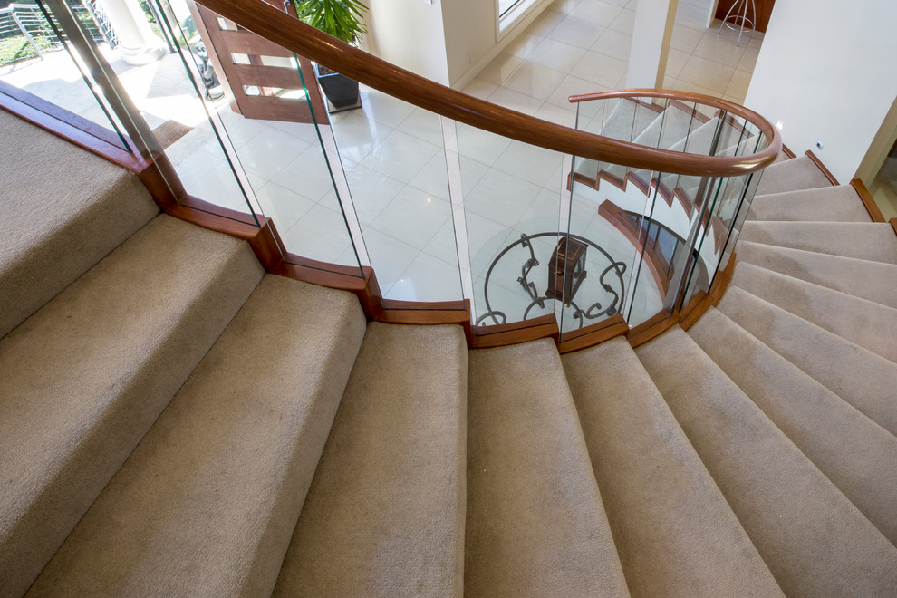 Design ideas for a large contemporary carpeted curved staircase in Sydney with carpet risers and glass railing.